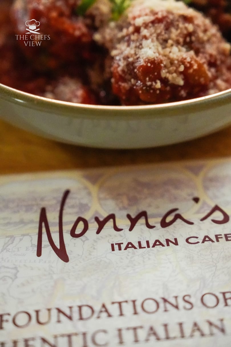 A bowl of Nonna's Italian Cafe meatballs with sauce and parmesan cheese, with the menu below.