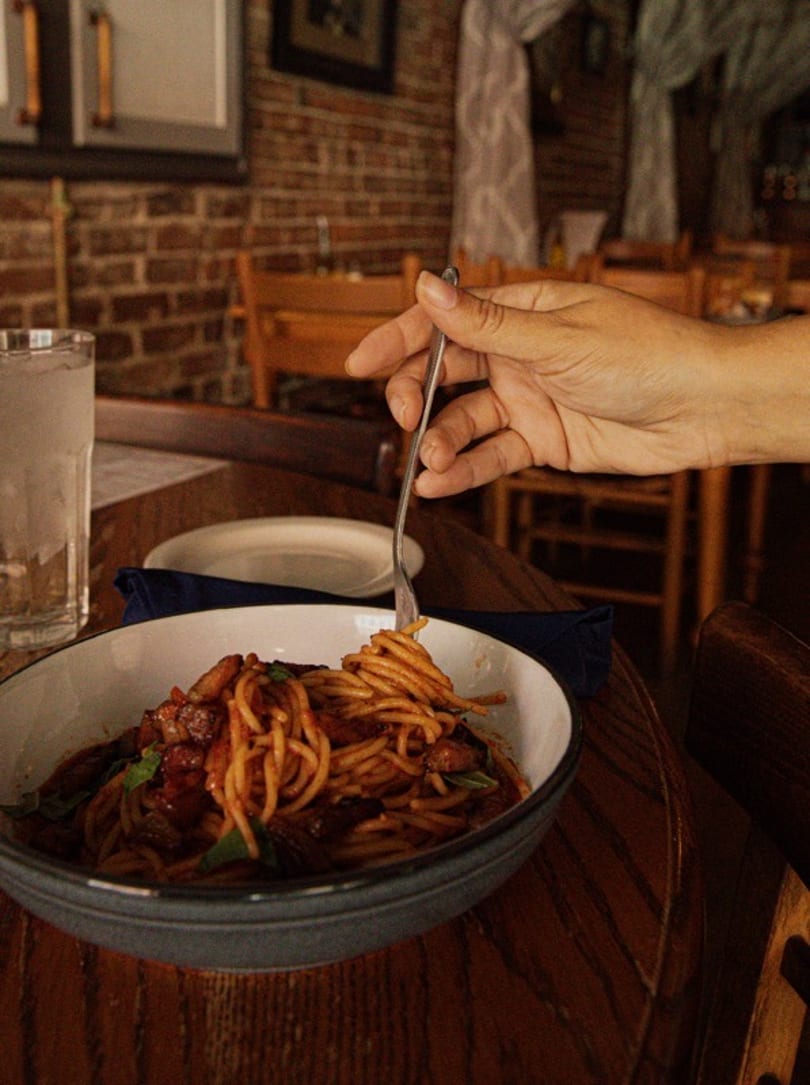 A hand twirls spaghetti with red sauce and meat onto a fork in a restaurant.