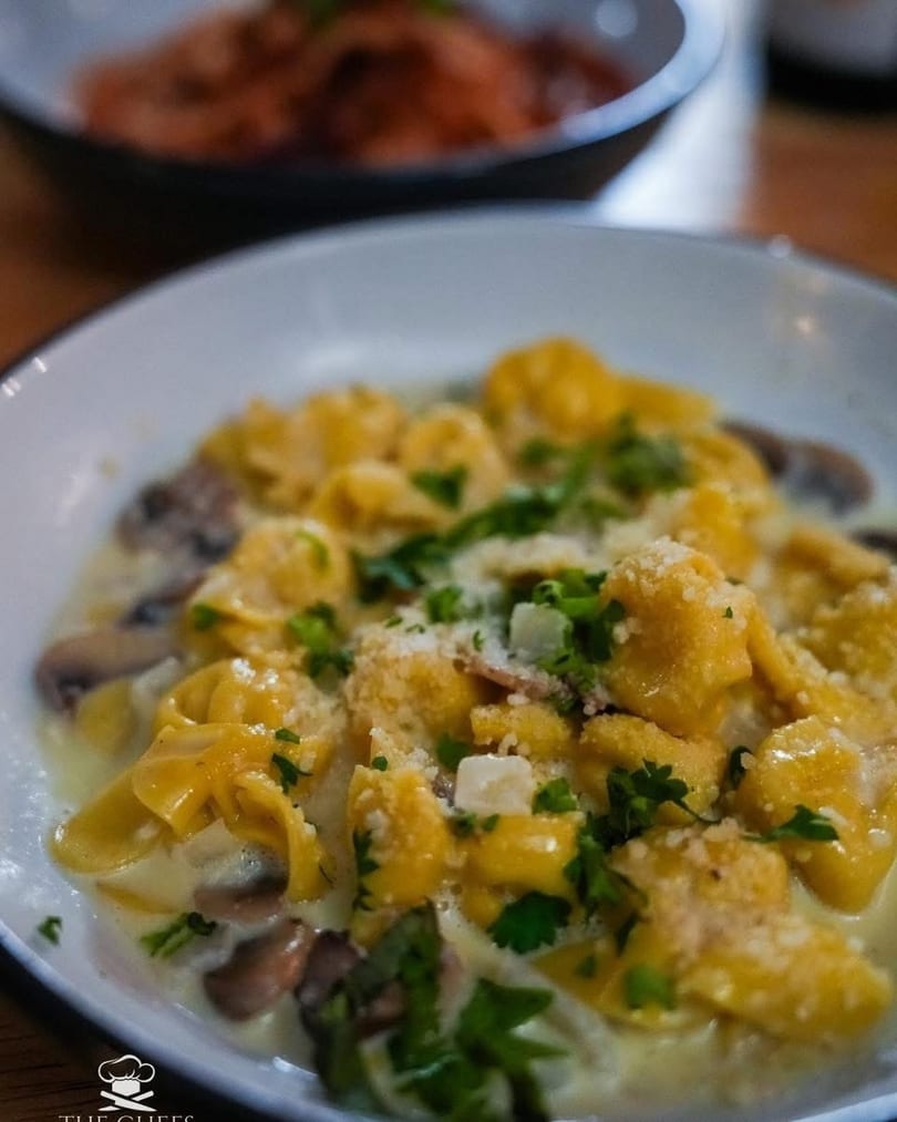 Close-up of tortellini in a creamy mushroom sauce, topped with parsley and grated cheese.